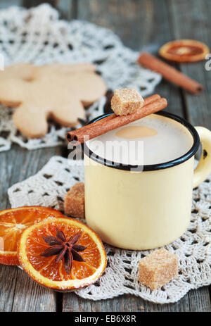 Heißer Kakao in einem alten gelben Becher auf einem Holztisch mit Stücken von Zucker, Zimtstangen und kandierten Orangenscheibe. Stockfoto