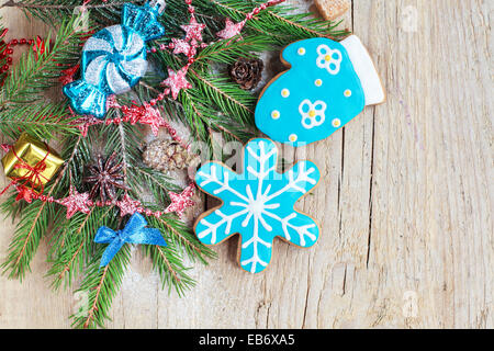 Hausgemachte Weihnachten Pfefferkuchen gemalt als blaue Schneeflocke und Fausthandschuh mit festlicher Dekoration auf dem hölzernen Hintergrund mit Tanne Stockfoto