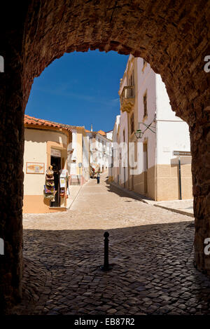 Portugal, Algarve, Silves, einer schmalen gepflasterten Straße in der Altstadt gesehen durch einen Torbogen in der Stadtmauer Stockfoto