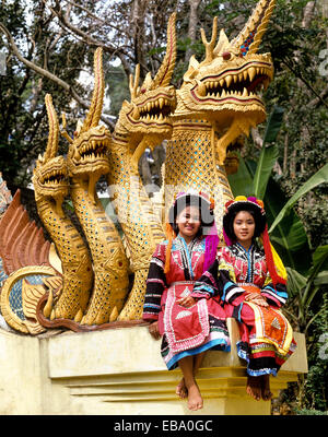 Zwei Lisu Hill Tribe Mädchen tragen Trachten und Kopfschmuck sitzt auf einer Naga Skulptur, buddhistische Tempel, Mae Sai Stockfoto