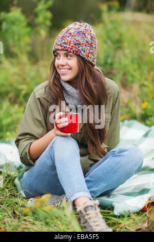 lächelnde junge Frau mit Tasse sitzt auf dem Campingplatz Stockfoto