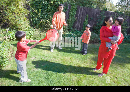 Junge Familie mit einem Schläger und Ball im Garten spielen, Stockfoto
