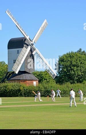 Land ikonischen Quintessenz England idyllische Dorf grünen Cricket Match Bowler Batsman & Fielder Mountnessing Post Mill Brentwood Essex Landschaft Stockfoto