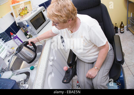 Weibliche Rollstuhlfahrer einen Wasserkocher mit Wasser in ihrer Küche nicht angepasst zu füllen, Stockfoto