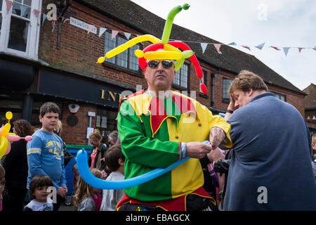 Bunt gekleidete Straße Entertainer macht Tierformen aus Luftballons für die Massen auf der Haslemere Charta Fair. Stockfoto