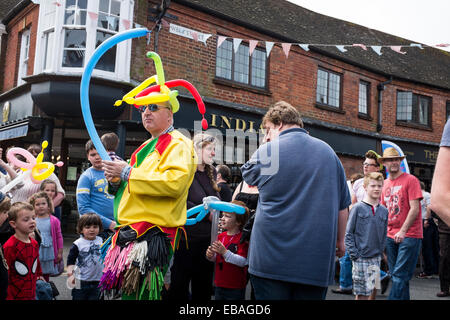 Bunt gekleidete Straße Entertainer macht Tierformen aus Luftballons für die Massen auf der Haslemere Charta Fair. Stockfoto