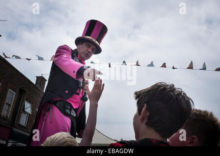 Straße Entertainer auf Stelzen, helle Kleidung deutet auf Kinder in der Menge auf der Charta Messe in Haslemere. Stockfoto