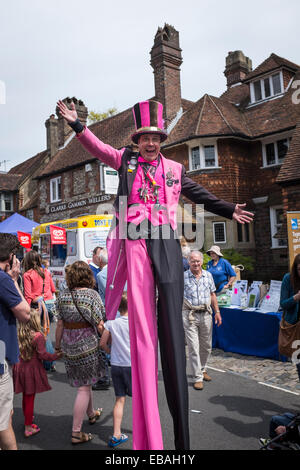 Straße Entertainer auf Stelzen, tragen helle Kleidung und einen Zylinderhut unterhält Andrang an der Charta Fair Haslemere. Stockfoto