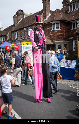 Straße Entertainer auf Stelzen, tragen helle Kleidung und einen Zylinderhut unterhält Andrang an der Charta-Messe in Haslemere. Stockfoto