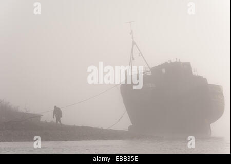 Loch Linnhe Schottland, Großbritannien. 28. November 2014. Eine einsame Gestalt bewundert die gestrandeten Fischerboot am Ufer des Loch Linnhe bei schweren Morgennebel Credit: Kenny Ferguson/Alamy Live News Stockfoto