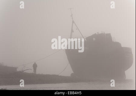 Loch Linnhe Schottland, Großbritannien. 28. November 2014. Eine einsame Gestalt bewundert die gestrandeten Fischerboot am Ufer des Loch Linnhe bei schweren Morgennebel Credit: Kenny Ferguson/Alamy Live News Stockfoto