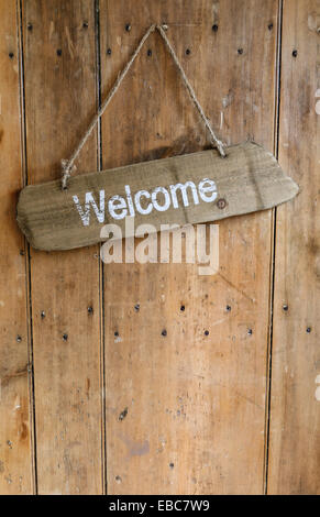 Willkommens-Schild hängt vom Nagel an einer alten Eiche rustikal aus Holz verwittert vor der Tür. Stockfoto