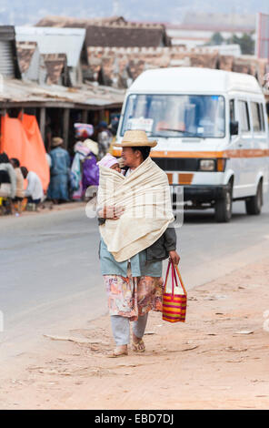 Eine lokale afrikanische Frau Spaziergänge entlang einer Straße in Antananarivo, oder Tana, Hauptstadt von Madagaskar, ihr Baby in eine Decke gewickelt tragen Stockfoto