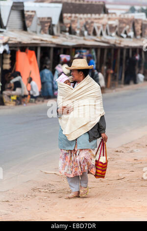 Eine lokale afrikanische Frau Spaziergänge entlang einer Straße in Antananarivo, oder Tana, Hauptstadt von Madagaskar, ihr Baby in eine Decke gewickelt tragen Stockfoto