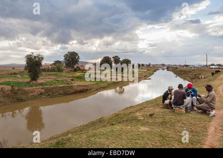 Lokale Lebensstil: Gruppe von vier lokalen afrikanischen Männer spielen Karten auf der Bank eines Bewässerungskanals in Antananarivo, oder Tana, Hauptstadt von Madagaskar Stockfoto