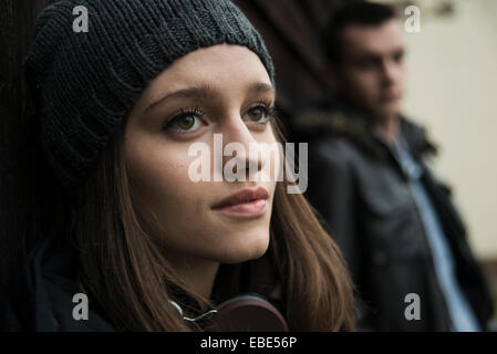 Close-up Portrait von Teenager-Mädchen im Freien, mit Hut und Kopfhörer um den Hals, mit jungen Mann im Hintergrund, Deutschland Stockfoto