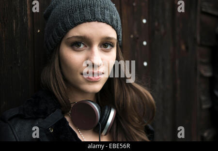 Close-up Portrait von Teenager-Mädchen im Freien, mit Hut und Kopfhörer um Hals, Blick in die Kamera und lächelnd, Deutschland