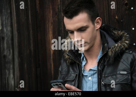 Nahaufnahme der junge Mann trägt die Jacke im Freien und Blick auf Handy, Deutschland Stockfoto