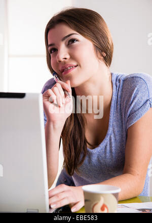 Junge Frau sitzt am Schreibtisch im Büro, Desktop-PC verwenden, auf der Suche nach oben und denken, Deutschland Stockfoto