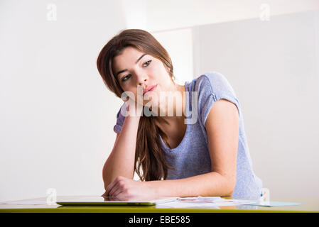 Junge Frau sitzt am Schreibtisch im Büro mit Tablet-Computer, Blick auf die Seite und denken, Deutschland Stockfoto