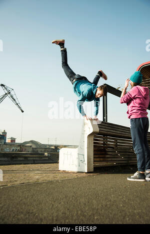 Teenager tun Handstand auf Bank im Freien, während der Teenager-Mädchen-Uhren, Industriegebiet, Mannheim, Deutschland Stockfoto