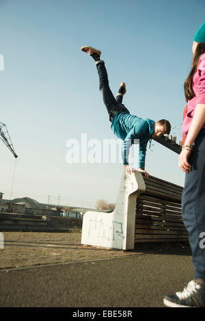 Teenager tun Handstand auf Bank im Freien, während der Teenager-Mädchen-Uhren, Industriegebiet, Mannheim, Deutschland Stockfoto