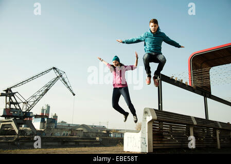 Teenager-Mädchen und jungen springen über Bank im Freien, Industriegebiet, Mannheim, Deutschland