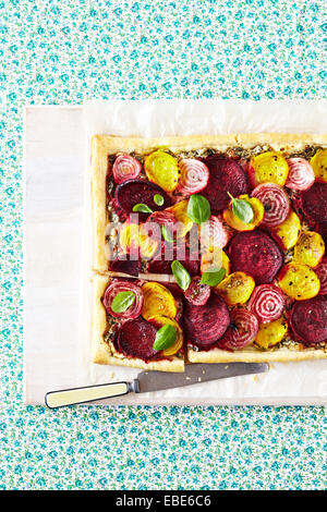 Rot, gelb und gestreiften Rüben-Tarte mit frischen Basilikum auf weißen Holzbrett mit Messer auf Floral Background, Studio gedreht Stockfoto