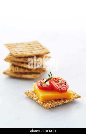 Cracker, garniert mit Cheddar-Käse, Tomatenscheiben und Kräuter mit Stapel der Cracker auf weißem Hintergrund, Studioaufnahme Stockfoto