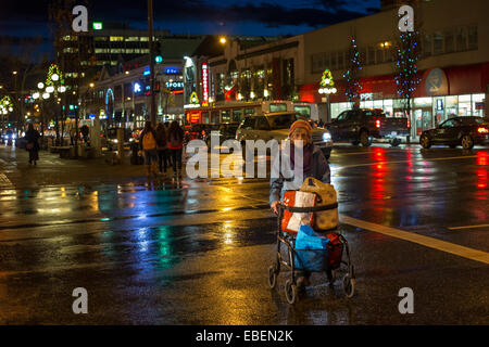 Ältere Frau mit Walker zu Fuß in der Innenstadt von Victoria auf regnerischen Nacht-Victoria, British Columbia, Kanada. Stockfoto