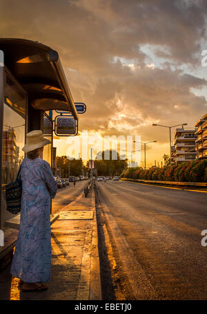 Eine Dame, die Wartezeit auf den Bus im Sonnenuntergang. Stockfoto