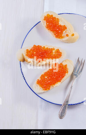 Sandwiches mit rotem Kaviar auf weißen Teller serviert mit Vintage Gabel über weißen Tisch. Ansicht von oben. Stockfoto