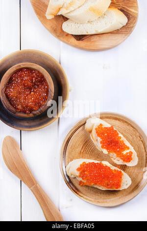 Schüssel und Sandwiches mit rotem Kaviar auf Keramikplatte über weißen Tisch serviert. Ansicht von oben. Serien ansehen Stockfoto