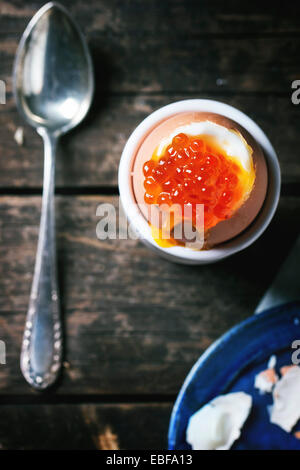 Frühstück mit wachsweiches Ei mit rotem Kaviar in weiß Eierbecher mit Vintage Löffel über alten Holztisch serviert. Serien ansehen Stockfoto