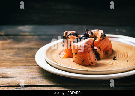 Lachs-Rollen mit schwarzem Kaviar, serviert auf Keramikplatte auf alten Holztisch. Stockfoto