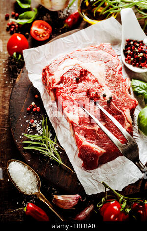 Rohes Rindersteak mit Fleischgabel und Zutaten auf hölzernen Hintergrund Stockfoto