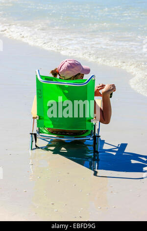 Eine Frau sitzt im Liegestuhl in der Nähe das ankommende Wasser des Golfs von Mexiko am Siesta Key Beach in Florida Stockfoto