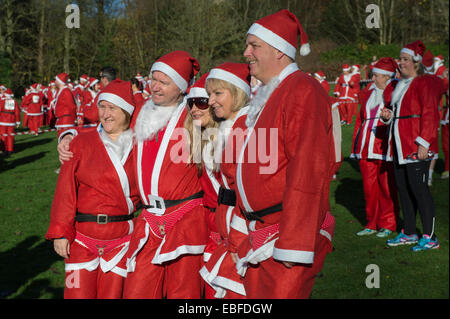 Menschen (Männer, Frauen und Kinder) Gekleidet in rot & weiß Vater Weihnachten Outfits mit Hüte & falsche Bärte, Stehen, warten Teil in der Großen Skipton Santa Fun Run, eine jährliche fundraising Charity Rennen vom Rotary Club - Aireville Park, Skipton Stadtzentrum, dem North Yorkshire, England, UK organisiert wird. Stockfoto