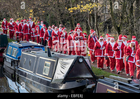 Vorderansicht des Menschen (Männer, Frauen und Kinder) in rot & weiß Vater Weihnachten Outfits gekleidet Gehen, Joggen, Laufen Vergangenheit Kanal Boote & die Teilnahme an der großen Skipton Santa Fun Run, eine jährliche fundraising Charity Rennen vom Rotary Club - Federn Zweig von Leeds Liverpool Canal Leinpfad, Skipton Stadtzentrum, dem North Yorkshire, England, Großbritannien organisiert. Stockfoto