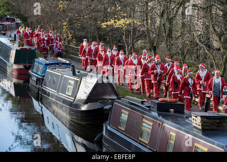 Vorderansicht des Menschen (Männer, Frauen und Kinder) in rot & weiß Vater Weihnachten Outfits gekleidet Gehen, Joggen, Laufen Vergangenheit Kanal Boote & die Teilnahme an der großen Skipton Santa Fun Run, eine jährliche fundraising Charity Rennen vom Rotary Club - Federn Zweig von Leeds Liverpool Canal Leinpfad, Skipton Stadtzentrum, dem North Yorkshire, England, Großbritannien organisiert. Stockfoto