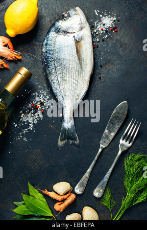 Köstlichen frischen Fisch und Meeresfrüchte auf dunkle Vintage-Hintergrund. Fisch, Herzmuscheln und Garnelen mit aromatischen Kräutern, Gewürzen & Gemüse Stockfoto