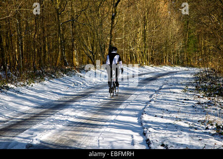 Eine männliche Radsportler, entlang einer Straße Schnee bedeckte Landschaft im Winter. Stockfoto