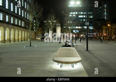 Bank mit Beleuchtung unter in St. Peter's Square, Manchester, England, UK das Kenotaph mit Flutlicht in der Ferne. Stockfoto