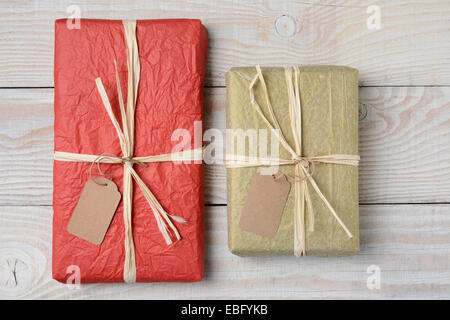Hohen Winkel Schuss zwei Geschenke auf einem weißen rustikalen Holztisch. Eingehüllt in zerknülltes Seidenpapier mit leeren Geschenkanhänger. Horizontale Stockfoto