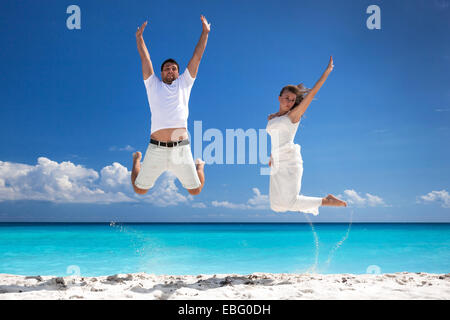 Glückliche Brautpaar sprang am Strand mit blauer Himmelshintergrund Stockfoto