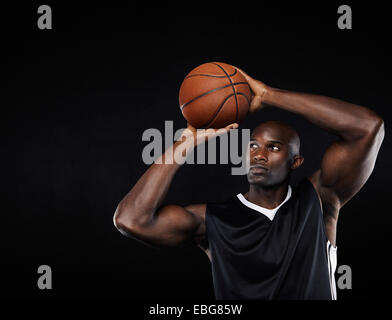 Young African American männliche Basketball-Spieler schießen auf den Reifen auf schwarzen Hintergrund Stockfoto