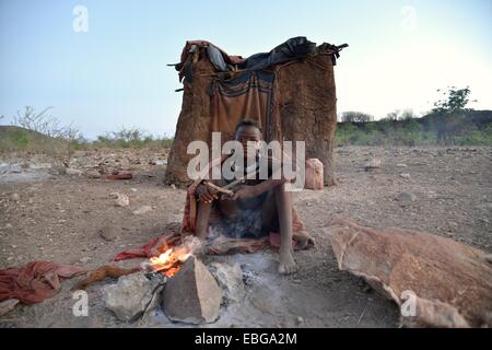 Junge Schäferin aus der Himba Leute sitzen am Lagerfeuer vor ihrer Hütte Ombombo, Kaokoland, Kunene, Namibia Stockfoto