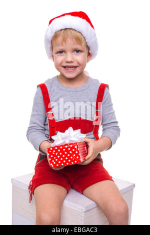 Kleines blondes Kind im roten Kostüm Zwerg hält Geschenkbox mit Schleife. Weihnachten. Studioportrait isoliert auf weißem Hintergrund Stockfoto