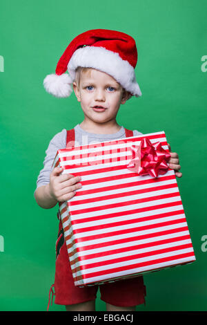 Weihnachtself halten große rote Geschenkbox mit Schleife. Santa Claus Helfer. Studio-Porträt auf grünem Hintergrund Stockfoto