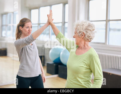 Ältere Frau geben hohe fünf zu ihrem persönlichen Trainer im Fitness-Studio. Aufgeregt, alte Frau Freude Gesundheit Erfolg mit ihrem Lehrer an Stockfoto